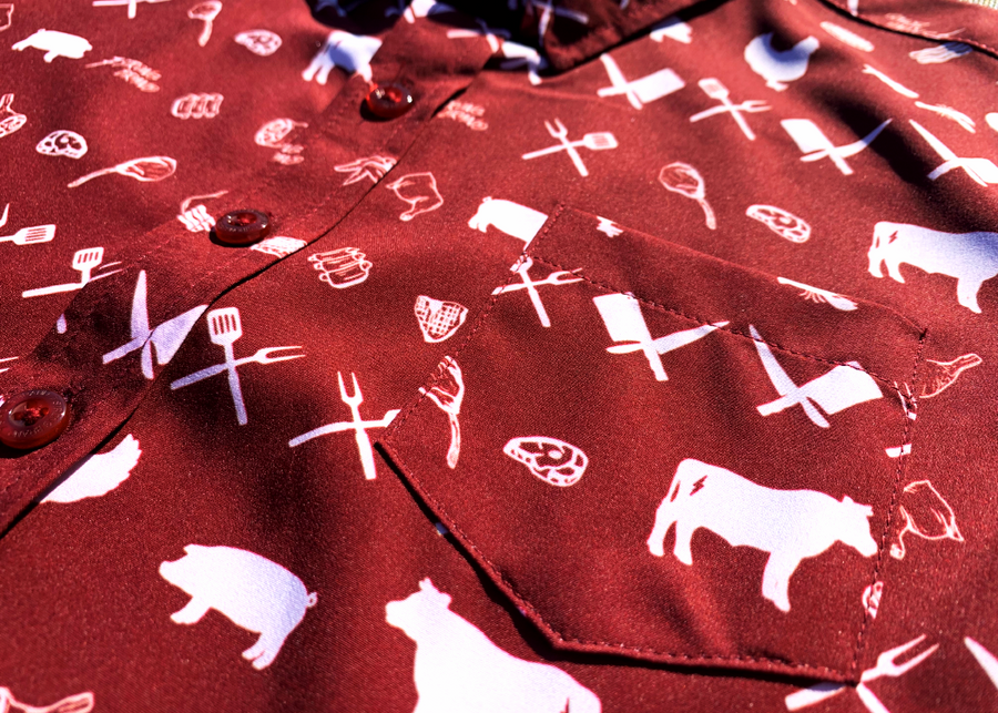 A midsection button close-up view of the 7-Strong youth "Smoke Show" button up, a deep maroon red colored shirt with rows of various barbecue and cookout related items and delicacies silhouetted in white.