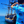 Load image into Gallery viewer, A medium close up on a youth model wearing the 7-Strong &quot;7-Seas&quot; shirt, a bright blue colored shirt with various nautical depictions such as islands, ships, mermaids, etc - drawn in a treasure map like fashion. Model is facing the water where a ship is docked, model is looking out towards it. 
