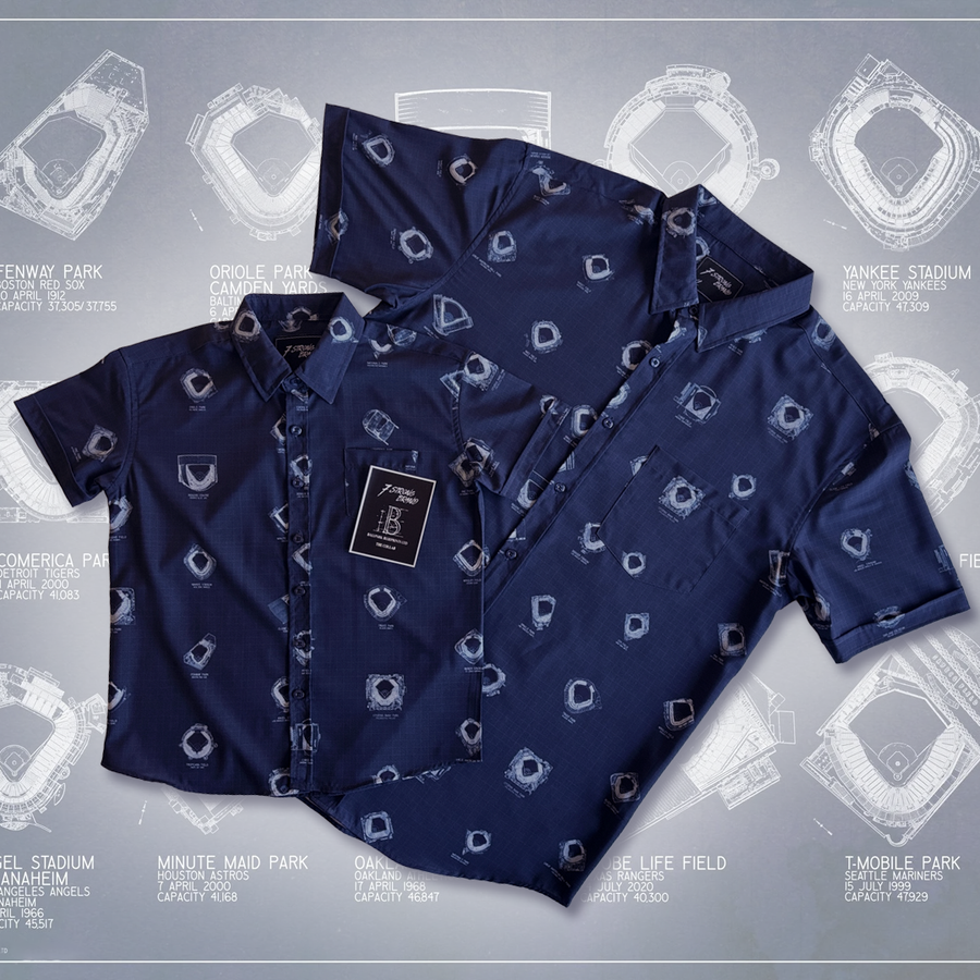 Adult and Youth versions of the 7-Strong Ballpark Blueprints short-sleeve button-down shirt displayed flat against a background featuring a large, faded architectural drawing of a baseball stadium. The navy fabric is decorated with white blueprint-like stadium illustrations, with a tag attached to the front pocket displaying the brand and product details.