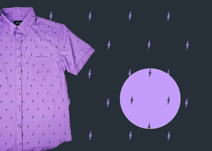 3/4 view of the 7-Strong Deep Lavender 7-Bolt short sleeve shirt, featuring black 7-bolts interspersed on a deep lavender background. The shirt is featured on a slate backdrop with lavender bolts. The bottom left features a detail circle showing the 7-bolt design up close.