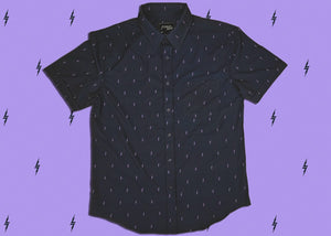 Full centered view of the 7-Strong Slate 7-Bolt short sleeve shirt, featuring lavender 7-bolts interspersed on a slate gray background. The shirt is featured on a lavender backdrop with black bolts