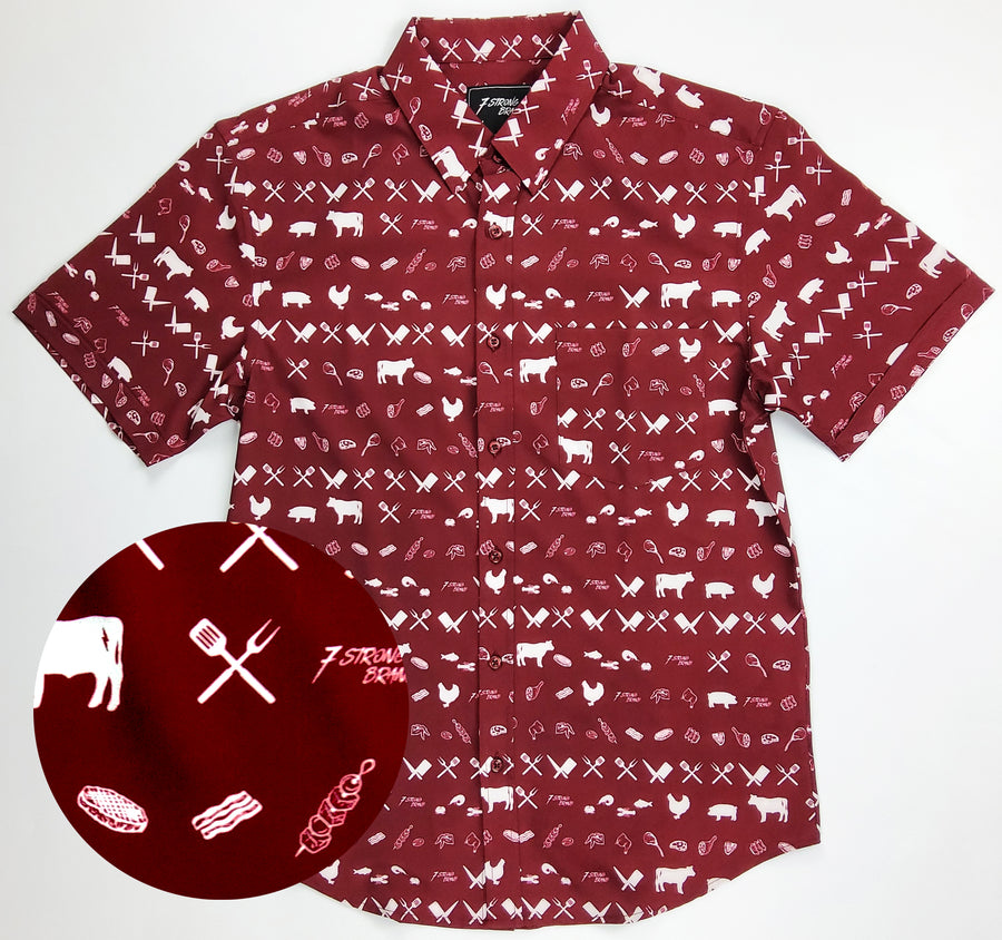A centered full view of the 7-Strong adult "Smoke Show" button up, a deep maroon red colored shirt with rows of various barbecue and cookout related items and delicacies silhouetted in white. The bottom right features a detail circle showing a close-up of elements in the design.