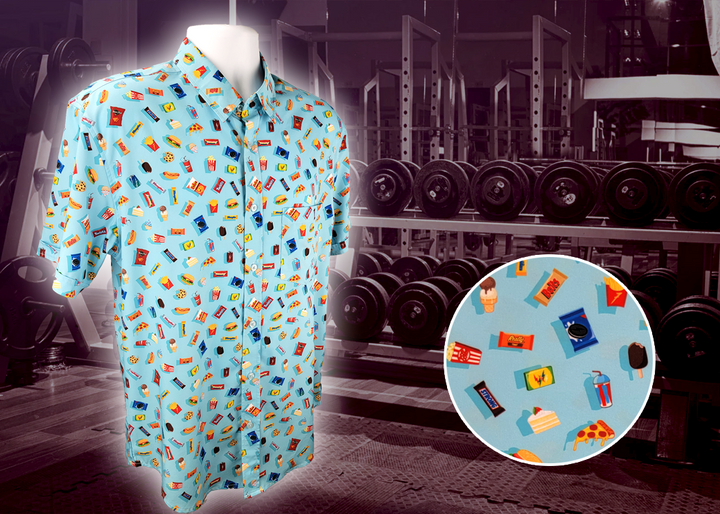 Full view of the 7-Strong "Cheat Day" adult button down featuring various snacks, treats, and fast food features on a light blue shirt. The shirt is displayed against a background of a gym weight rack. Bottom right corner has a close up detail circle showing some of the design features upclose. 