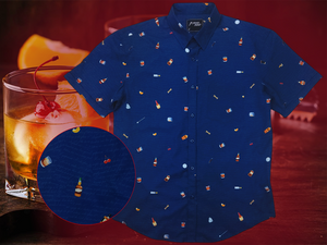 Full layout of "Call Me Old Fashioned" adult short sleeve button-down. Features elements of an Old Fashioned cocktail (bottle of bourbon, glasses, oranges, stirrers, and ice) against a blue background which faintly spells out an Old Fashioned recipe. Shirt is on a background featuring a finished Old Fashioned and has a detail circle in the bottom corner showing design detail. 
