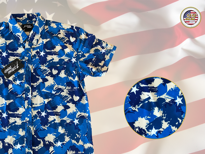 3/4 Full view close up of the 7-Strong "Service Stars" Adult button-up, featuring blue and creme colored camouflage with white weathered stars throughout. The shirt is featured against a waving U.S. Flag faded into the background. Top right is the 22 Flag Co logo, bottom left is a detail circle showing a close up of the camouflage and star design. 