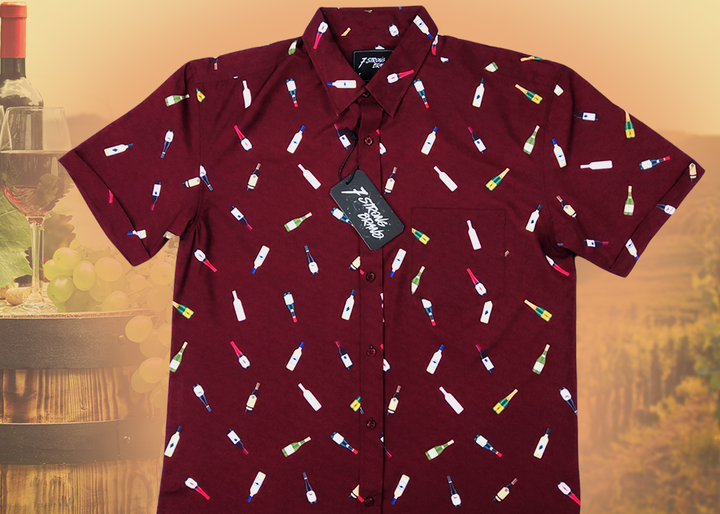 Full view of the 7-Strong "Pour Decisions" button up - deep red in color with various shaped and colored wine bottles patterned throughout in varying directions. Shirt is displayed against a sepia toned vineyard background. 