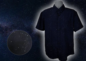 Full view of the short-sleeve Stargazer button down shirt. A deep navy blue shirt with constellation star patterns throughout. The shirt is displayed against a night sky full of stars. Bottom left corner shows a detail circle showcasing the constellation design.