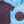Load image into Gallery viewer, 3/4 full view of the 7-Strong &quot;Aye Poppy&quot; button down, featuring an array of red poppys with white sprigs on a deep navy blue shirt. The shirt is displayed against a partly cloudy sky. The bottom right has a detail circle featuring a close up of the design. 
