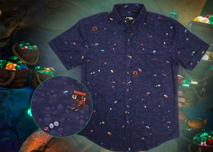 Full view shot of the 7-Strong "Mine Train" adult button up. Shirt is a deep purple with a rock quarry depicting ghosted design showcasing various colors of gemstones and mine train carts throughout. The shirt itself is displayed against a background of a mine shaft and various gems found in buckets. Bottom left corner has a detail circle depicting a close up of the shirt design. 