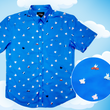 Load image into Gallery viewer, Full shot of the 7-Strong &quot;When Pigs Fly&quot; shirt, showcasing various pigs and meats flying against a blue, muted cloud background. Shirt is displayed against a background of cartoon clouds. Bottom right corner shows a circle showing the details of the pigs drawn on the shirt. 
