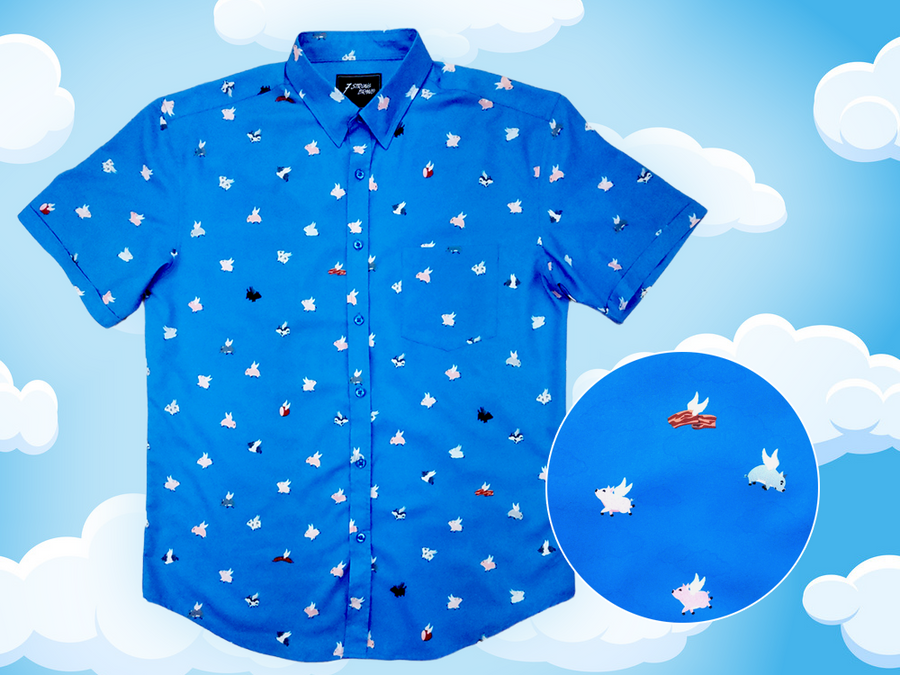 Full shot of the 7-Strong "When Pigs Fly" shirt, showcasing various pigs and meats flying against a blue, muted cloud background. Shirt is displayed against a background of cartoon clouds. Bottom right corner shows a circle showing the details of the pigs drawn on the shirt. 