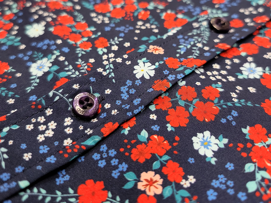Close up of the middle button portion of the 7-Strong "Aye Poppy" button down which features red poppies with white sprigs against a deep navy blue background. 
