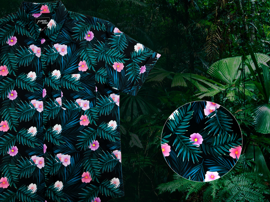3/4 view of the Adult 7-Strong "Tropic Like It's Hot" button down shirt - a black shirt with distinctive green palm trees and pink, white, and purple flowers peering out from behind the palms. Shirt is shown on a tropical rainforest background. Bottom right corner features a circle that details the flowers and palms designed on the shirt in close up. 