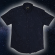 Load image into Gallery viewer, Full view of the short-sleeve Stargazer button down shirt. A deep navy blue shirt with constellation star patterns throughout. The shirt is displayed against a night sky full of stars.
