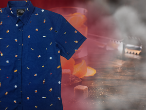 3/4 layout, right justified of "Call Me Old Fashioned" adult short sleeve button-down. Features elements of an Old Fashioned cocktail (bottle of bourbon, glasses, oranges, stirrers, and ice) against a blue background which faintly spells out an Old Fashioned recipe. Shirt is on a background featuring a finished Old Fashioned.