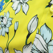 Load image into Gallery viewer, Close up mid drift button view of the 7-Strong &quot;Late Bloomer&quot; adult button down - a yellow background shirt with white and blue flowers patterned all over it. Shirt is against a blue tropical sky with palm trees in the distance. 
