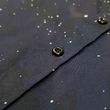 Load image into Gallery viewer, Midsection view of the short-sleeve Stargazer button down shirt. A deep navy blue shirt with constellation star patterns throughout. The shirt is displayed against a night sky full of stars.

