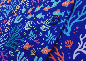 Close up mid torso shot of the 7-Strong "Coral of the Story" adult button down shirt. Color of the shirt is blue with vibrant purple, teal, orange sea life imagery - particularly fish and coral reef. 
