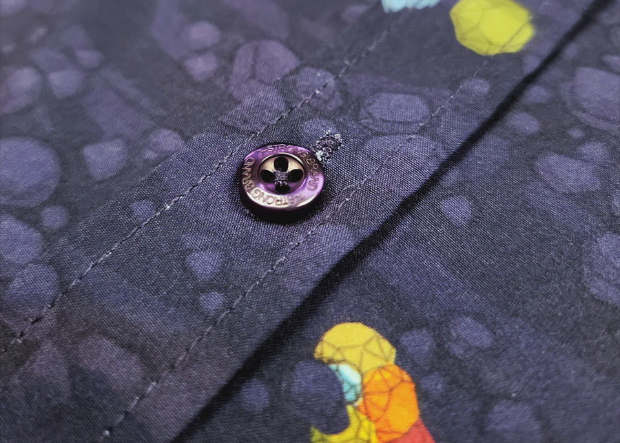 Close up shot of the button midsection of the 7-Strong Mine Train button down depicting various colored gemstones shining in a mine shaft rock quarry of deep purple color. 