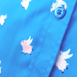 Load image into Gallery viewer, Close upshot of midsection on the 7-Strong &quot;When Pigs Fly&quot; shirt, showcasing various pigs and meats flying against a blue, muted cloud background. Shirt is displayed against a background of cartoon clouds.

