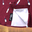 Load image into Gallery viewer, Bottom sweep tag view of the adult 7-Strong &quot;Pour Decisions&quot; button up - deep red in color with various shaped and colored wine bottles patterned throughout in varying directions. Shirt is displayed against a sepia toned vineyard background. 
