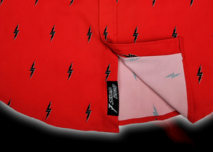 Bottom sweep tag view of the 7-Strong Red 7-Bolt short sleeve shirt, featuring black 7-bolts with a white drop shadow interspersed on a red background. The shirt is featured on a red lightning storm backdrop.