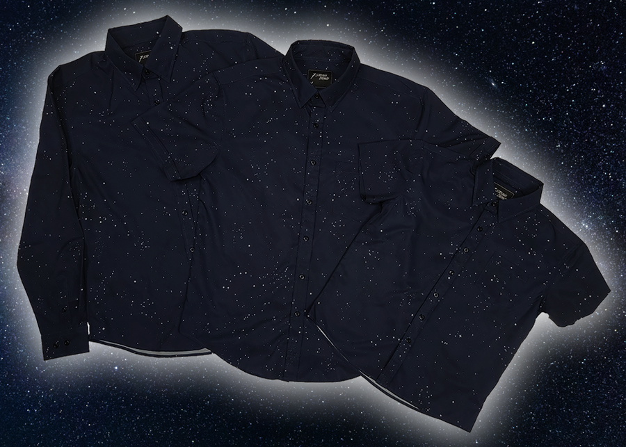 Full view of the long-sleeve, and short-sleeve adult and youth Stargazer button down shirts overlapping one another. A deep navy blue shirt with constellation star patterns throughout. The shirt is displayed against a night sky full of stars.