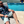 Load image into Gallery viewer, Male adult model sitting in a beach recliner by the pool wearing the 7-Strong &quot;Tropic Like It&#39;s Hot&quot; adult button up. Shirt is black with detailed green palms, matches with white, pink, and purple flowers peering throughout the shirt - paired with light mint shorts. 
