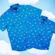 Load image into Gallery viewer, Full shot of the adult and youth 7-Strong &quot;When Pigs Fly&quot; button down shirt, showcasing various pigs and meats flying against a blue, muted cloud background. Shirt is displayed against a background of cartoon clouds.
