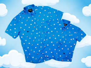 Full shot of the adult and youth 7-Strong "When Pigs Fly" button down shirt, showcasing various pigs and meats flying against a blue, muted cloud background. Shirt is displayed against a background of cartoon clouds.