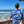 Load image into Gallery viewer, Male model, back to camera holding a surfboard overlooking the ocean while wearing the 7-Strong &quot;Let &#39;Er Riptipe&quot; Adult button down shirt, featuring an array of indigo and purple waves with whitecaps all over. 
