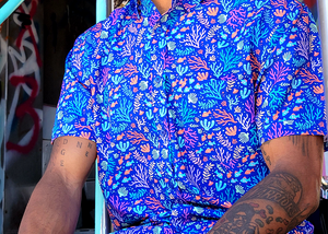 Mid torso shot of a male model wearing the 7-Strong "Coral of the Story" adult button down shirt. Color of the shirt is blue with vibrant purple, teal, orange sea life imagery - particularly fish and coral reef.