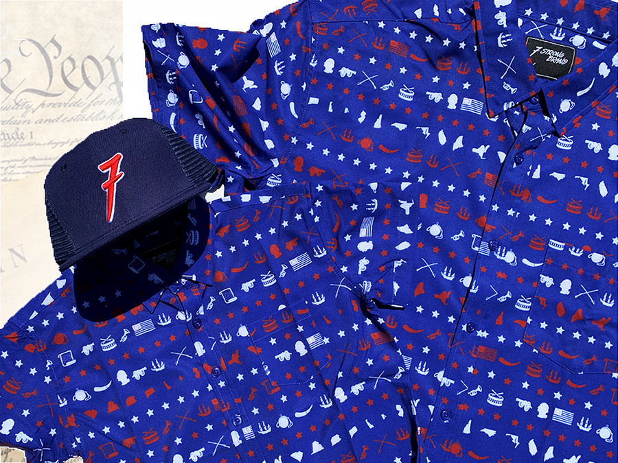 Full, front faing shot of the 7-Series trucker hat, showcasing its all navy blue look, back mesh panel, red puffed embroidered 7 with white outline, against a background of the Declaration of Independence, laid on top of both the youth and adult versions of the 1776 royal blue shirt with Americana icons striped throughout .