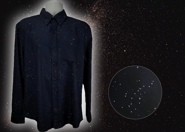 Full view of the long-sleeve Stargazer button down shirt. A deep navy blue shirt with constellation star patterns throughout. The shirt is displayed against a night sky full of stars. Bottom right corner shows a detail circle showcasing the constellation design. 