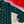 Load image into Gallery viewer, 3/4 full view of the long-sleeve 7-Strong &quot;Oh, Christmas Treat&quot; shirt - a green, christmas sweater-like background with columns of various white Christmas tree shaped cakes with red garland, some whole, some bitten. The shirt is displayed against a red, snowing background with a similar parted cake. 
