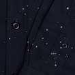 Load image into Gallery viewer, Midsection and draping sleeve view of the long-sleeve Stargazer button down shirt. A deep navy blue shirt with constellation star patterns throughout. The shirt is displayed against a night sky full of stars. 
