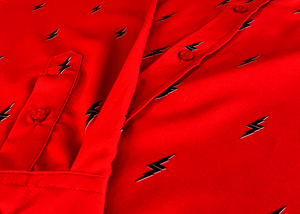 Close up mid button and long sleeve view of the 7-Strong Red 7-Bolt long sleeve shirt, featuring black 7-bolts with a white drop shadow interspersed on a red background. The shirt is featured on a red lightning storm backdrop.
