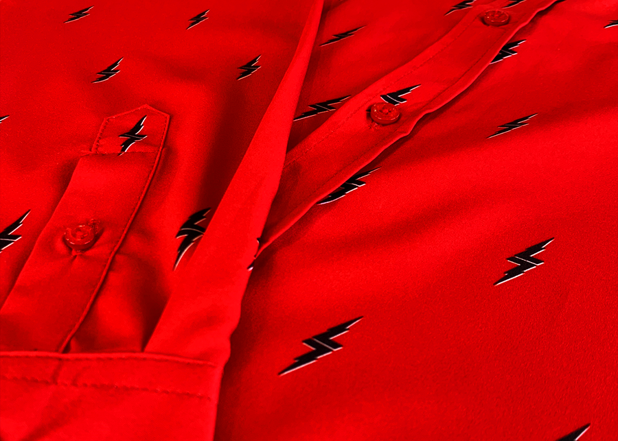 Close up mid button and long sleeve view of the 7-Strong Red 7-Bolt long sleeve shirt, featuring black 7-bolts with a white drop shadow interspersed on a red background. The shirt is featured on a red lightning storm backdrop.