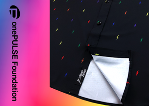 Close up, focusing on sweep tag portion of long sleeve adult button down shirt, black as base color and adorned with multicolored version of our 7-Bolt design. Shirt is on a multicolor gradient-like background, and on along the side left, the logo for onePULSE Foundation, our cause collection partner.