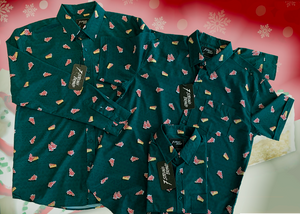 Full view of the long-sleeve, adult and youth short-sleeve versions of the  7-Strong "Oh, Christmas Treat" shirt overlapping each other on display - a green, christmas sweater-like background with columns of various white Christmas tree shaped cakes with red garland, some whole, some bitten. The shirt is displayed against a red, snowing background with a similar parted cake. 