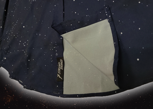 Bottom sweep tag portion view of the long-sleeve Stargazer button down shirt. A deep navy blue shirt with constellation star patterns throughout. The shirt is displayed against a night sky full of stars. 