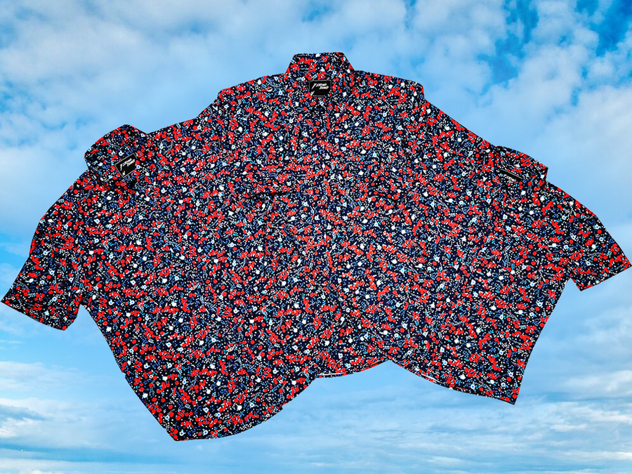 Full, overlapping view of the three versions (adult, youth, and long sleeve) of the 7-Strong "Aye Poppy" button down, featuring an array of red poppys with white sprigs on a deep navy blue shirt. The shirt is displayed against a partly cloudy sky.