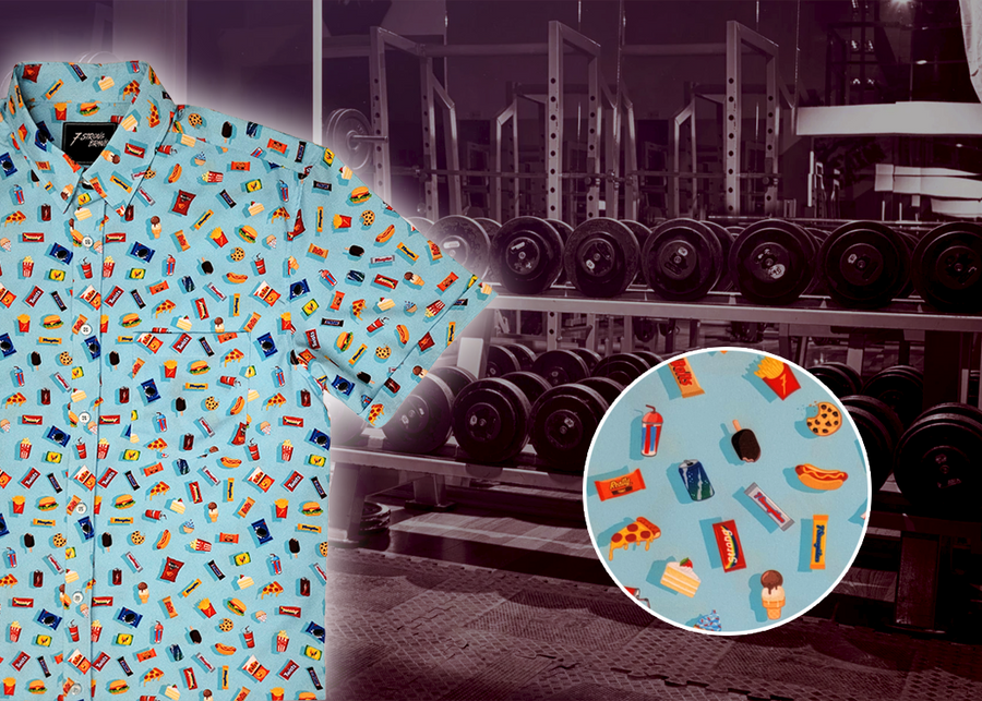 3/4 view of the 7-Strong "Cheat Day" youth button down featuring various snacks, treats, and fast food features on a light blue shirt. The shirt is displayed against a background of a gym weight rack. Bottom right corner has a close up detail circle showing some of the design features up close.