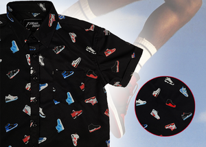 3/4 view of the youth short sleeve version of "Got 'Em!" The button down features various athletic fashion sneakers in an 80bit format arranged all over a black shirt. The shirt is featured against a background of a basketball player jumping in air, noticeable sneakers being worn. Bottom right corner features a detail circle showing the various shoes up close. 