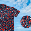 Load image into Gallery viewer, 3/4 full view of the youth 7-Strong &quot;Aye Poppy&quot; button down, featuring an array of red poppys with white sprigs on a deep navy blue shirt. The shirt is displayed against a partly cloudy sky. The bottom right has a detail circle featuring a close up of the design. 
