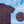 Load image into Gallery viewer, 3/4 full view of the youth 7-Strong &quot;Aye Poppy&quot; button down, featuring an array of red poppys with white sprigs on a deep navy blue shirt. The shirt is displayed against a partly cloudy sky. The bottom right has a detail circle featuring a close up of the design. 
