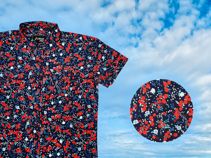 3/4 full view of the youth 7-Strong "Aye Poppy" button down, featuring an array of red poppys with white sprigs on a deep navy blue shirt. The shirt is displayed against a partly cloudy sky. The bottom right has a detail circle featuring a close up of the design. 
