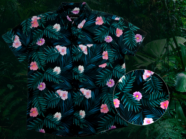 Full view of the Youth 7-Strong "Tropic Like It's Hot" button down shirt - a black shirt with distinctive green palm trees and pink, white, and purple flowers peering out from behind the palms. Shirt is shown on a tropical rainforest background. Bottom right of the photo shows a circle detailing the flowers and palms on the shirt in closeup. 