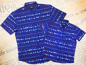 A full representation of both 7-Strong's youth and adult 1776 button down shirts, laid over top each other, against a Declaration of Independence background. Shirt is royal blue with stripes of various Americana icons, including the original 13 colonies and revolutionary war items.