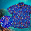 Load image into Gallery viewer, Full view shot of the 7-Strong &quot;Coral of the Story&quot; youth button down shirt. Color of the shirt is blue with vibrant purple, teal, orange sea life imagery - particularly fish and coral reef. The shirt is shown against an underwater background showcasing coral. In the left corner, there is a close up circle showcasing the details of the shirt. 

